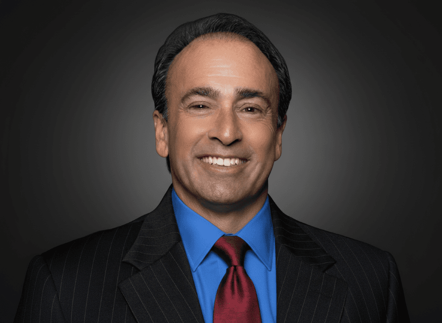 Professional headshot of a smiling man in a pinstripe suit, blue shirt, and red tie.